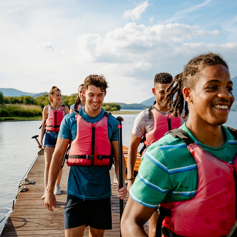 hero image high summer of a group in lifejackets walking back on the pier with kayak rowers